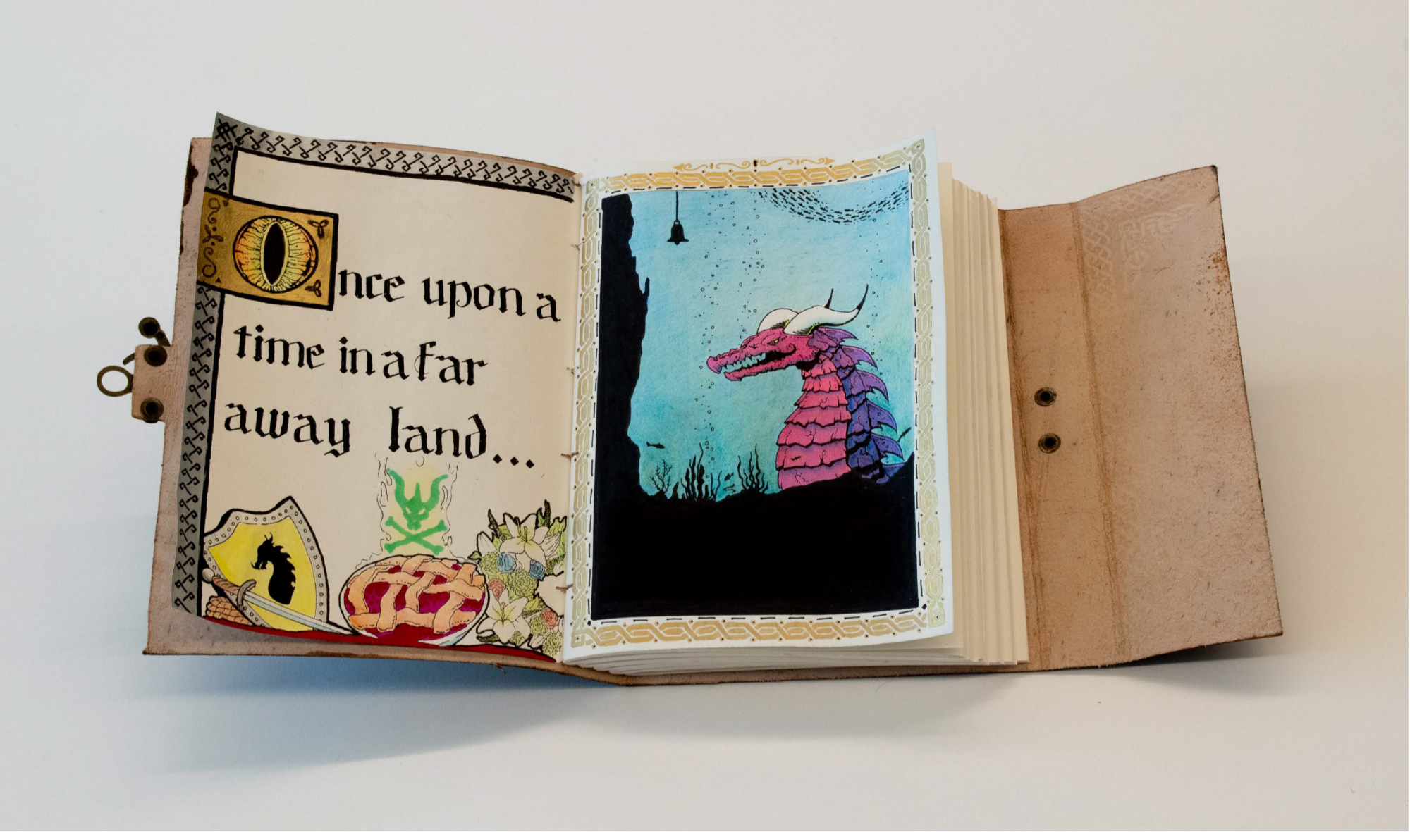 leather-bound book with illuminated letter and pencil drawing of dragon